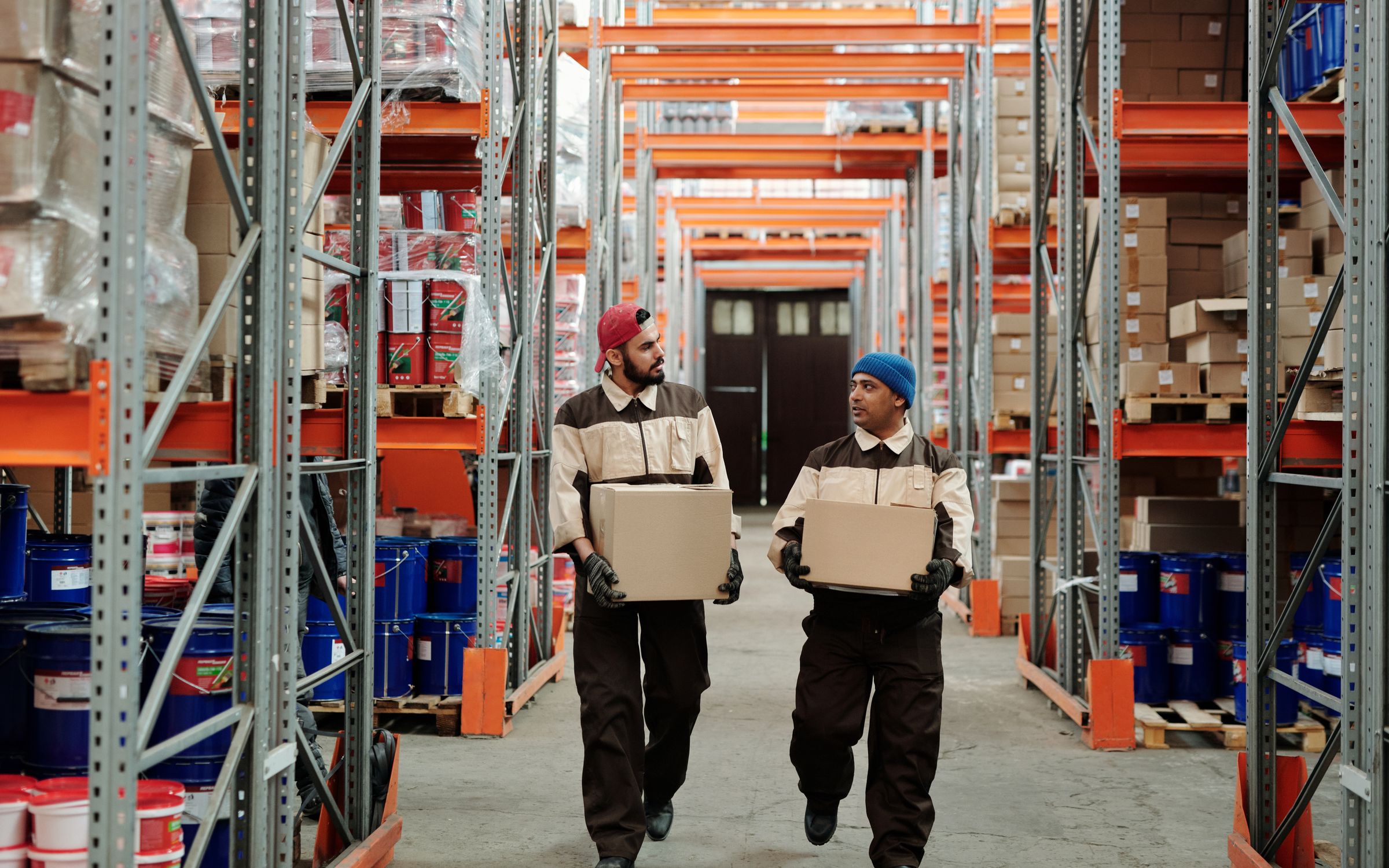Warehouse operatives carrying cartons through a racked storage aisle